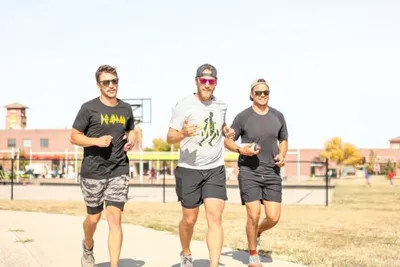 Three men jogging together outdoors near a brick building on a sunny day