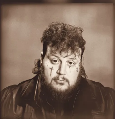 Heavyset bearded man with cross face tattoos in a sepia-toned portrait