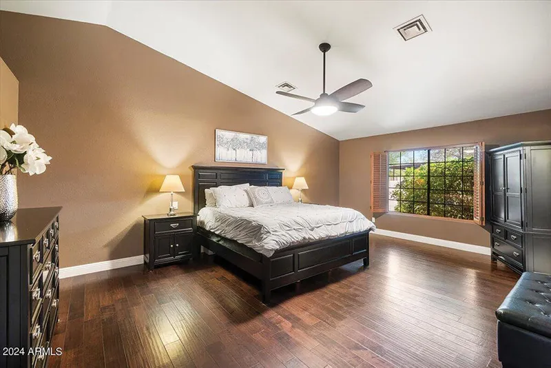 Spacious bedroom with dark wood furniture, hardwood floors, vaulted ceiling, and ceiling fan