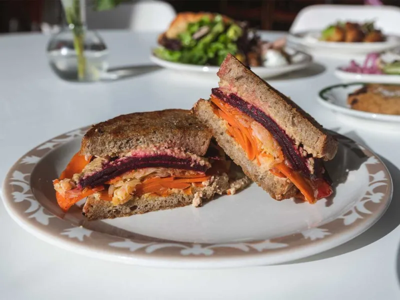 Halved vegetable sandwich on dark bread with beets and carrots on a patterned plate