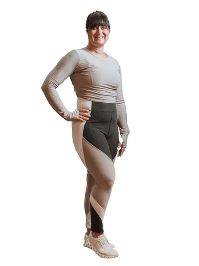 Smiling woman in beige long-sleeve crop top and color-block leggings poses against white background