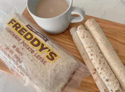 Freddy's Homemade Potato Lefse package beside rolled lefse and a cup of coffee on a wooden board