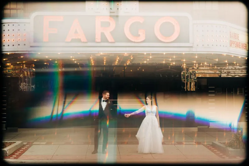 Bride and groom holding hands beneath the lit Fargo Theatre marquee, with rainbow lens flare