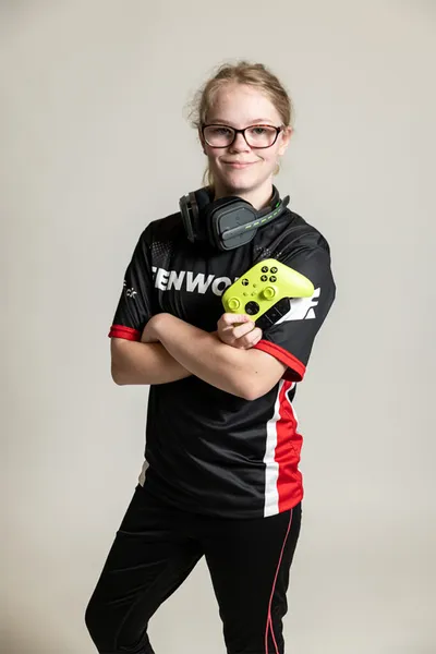 Young esports athlete holding a neon yellow game controller with headphones around her neck